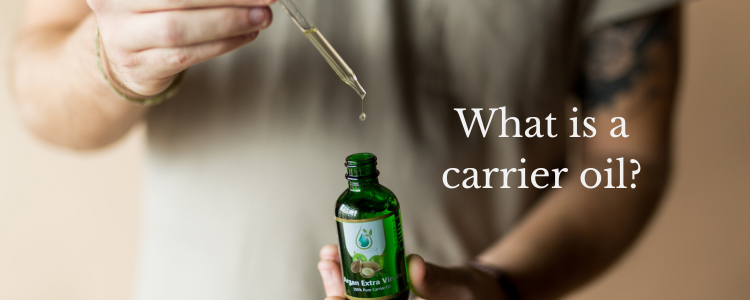 Person torso shown while holding a bottle of Argan oil holding a dropper pipette over the bottle with a single drop falling from pipette to bottle. What are carrier oils?